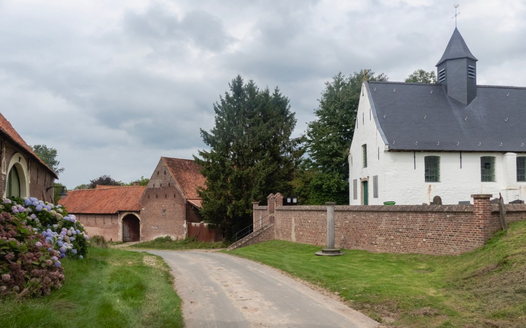 Een mooie weg door een dorpje, met een kerk en een baksten boerderij