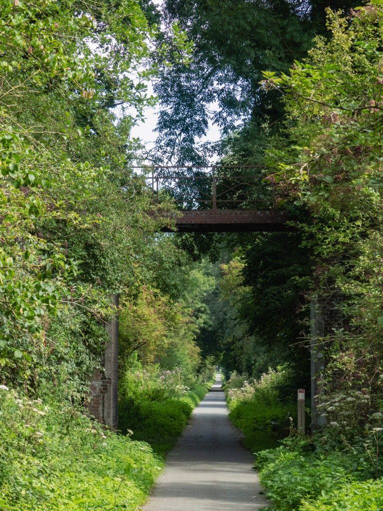 Fietspad die een oude spoorwegberm was - groen langs de twee kanten en een verroeste brug erover